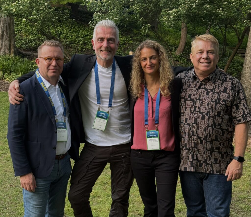 Four people wearing EarthX badges stand together on a lawn in front of trees.